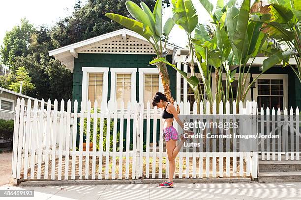 young woman stretching leg by picket fence - quadriceps muscle stock pictures, royalty-free photos & images