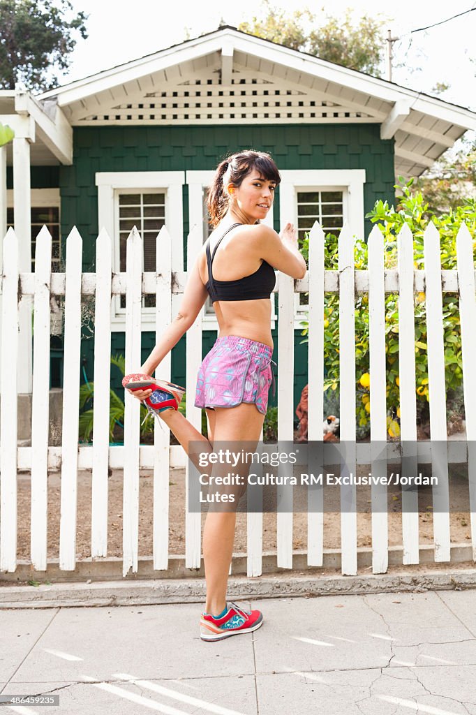 Young woman stretching leg by picket fence