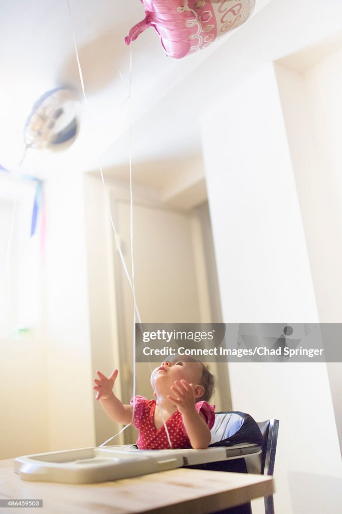 Toddler girl in highchair looking up at balloons