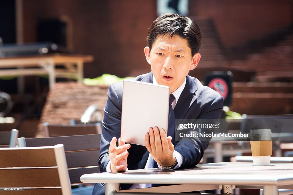 Japanese office worker reads shocking news on tablet outdoors