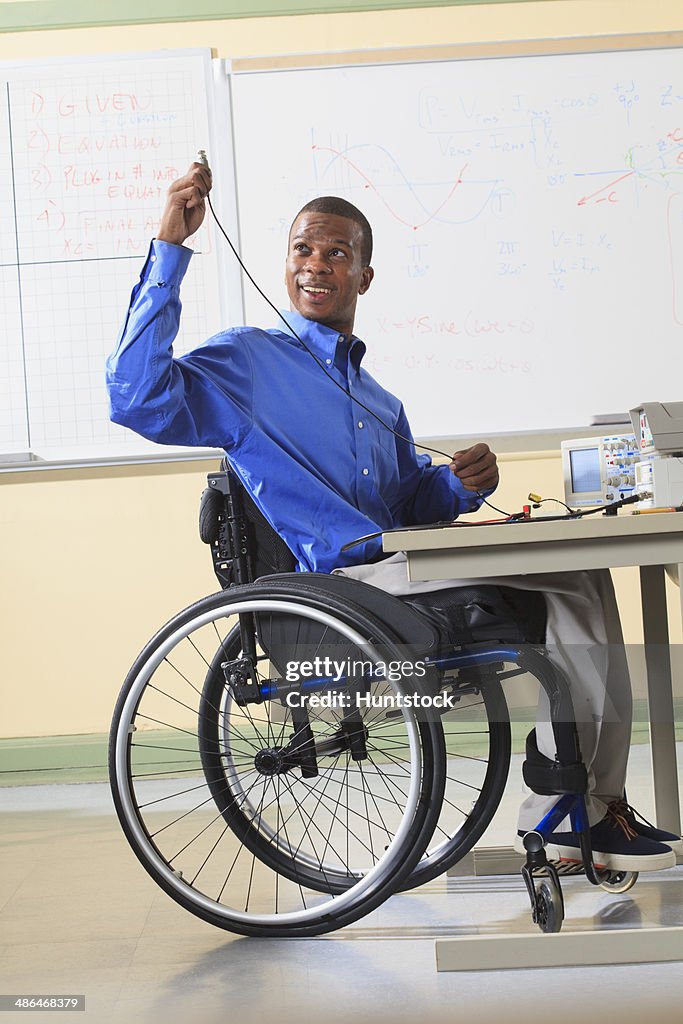 Engineering student sitting in a wheelchair preparing lab experiment with oscilloscope and electronic prototyping breadboard