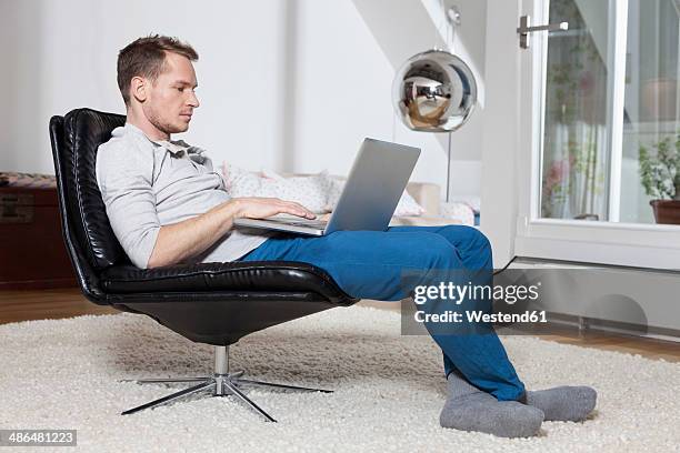 man at home relaxing in armchair with laptop - profile laptop sitting stock-fotos und bilder