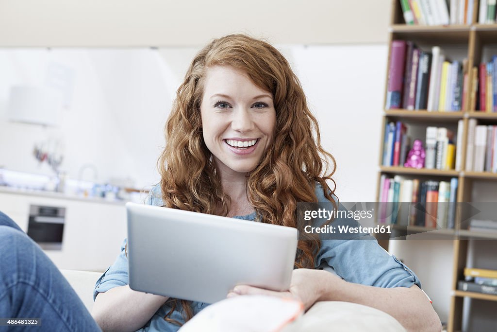 Portrait of young woman relaxing with tablet computer on a couch in her apartment