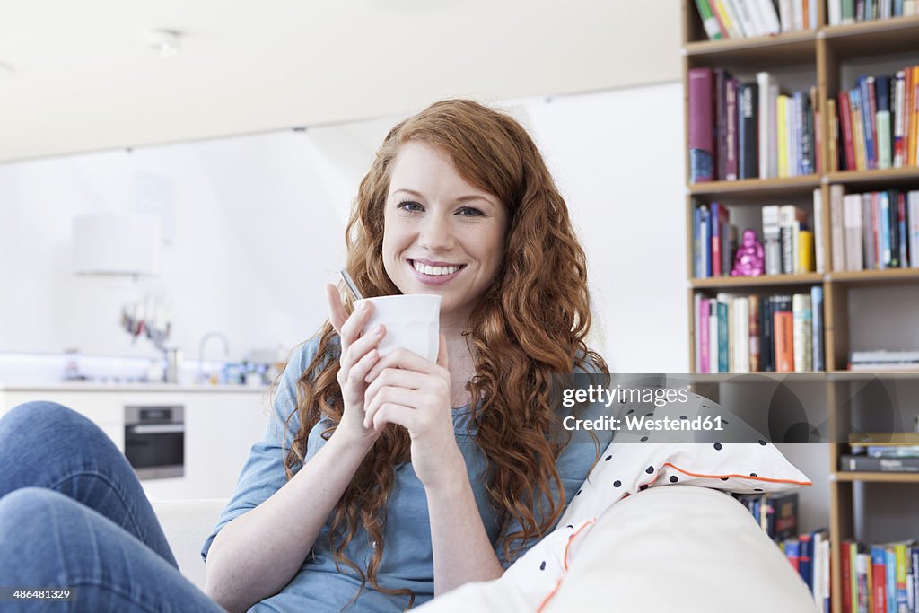 Portrait of young woman relaxing with cup of coffee on a couch in her apartment