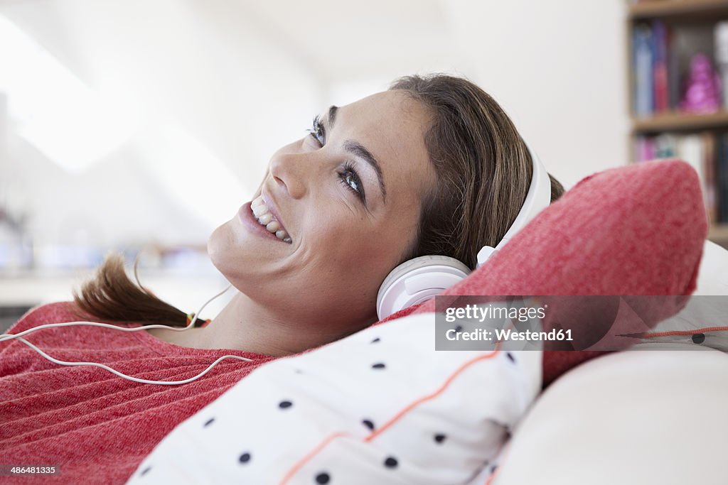 Portrait of woman with headphones lying on a couch in her apartment