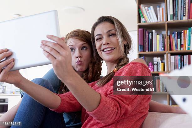 two young female friends taking a picture of themseves with tablet computer - kussmund stock-fotos und bilder