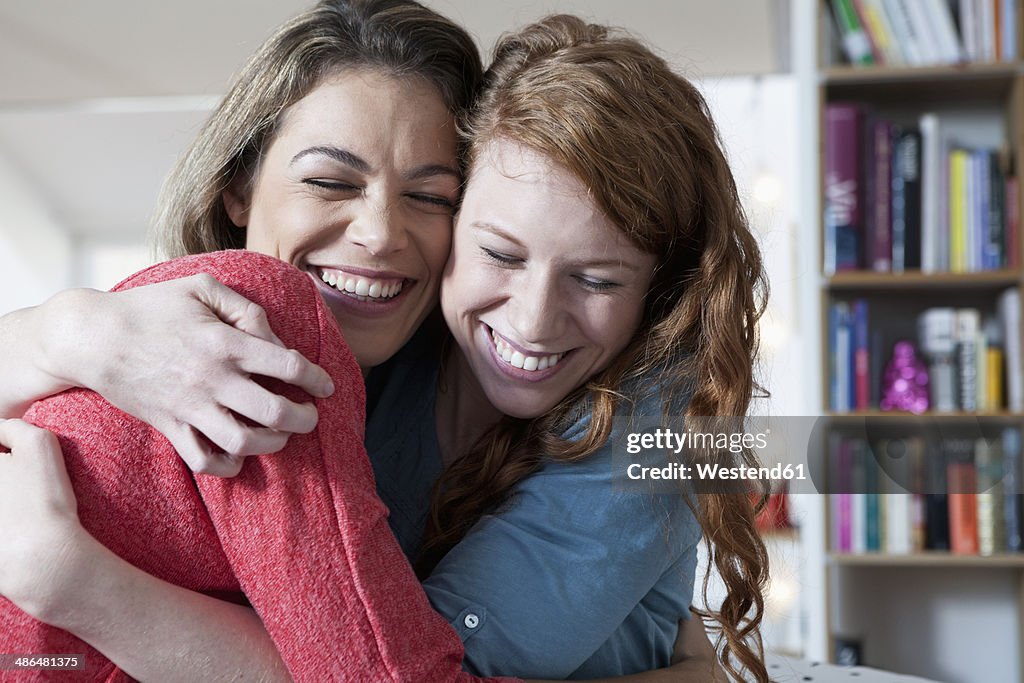 Two young female friends at home embracing