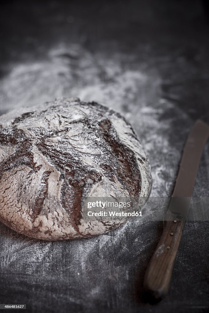 Rye-Spelt-Malt loaf, flour and bread knife on wooden table