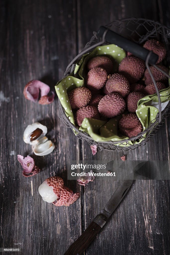 Wire basket, knife and whole and peeled lychees on dark wooden table