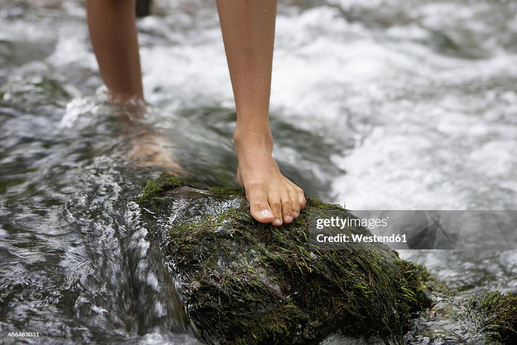 Austria, Salzkammergut, Mondsee, feet of teenage girl crossing a brook