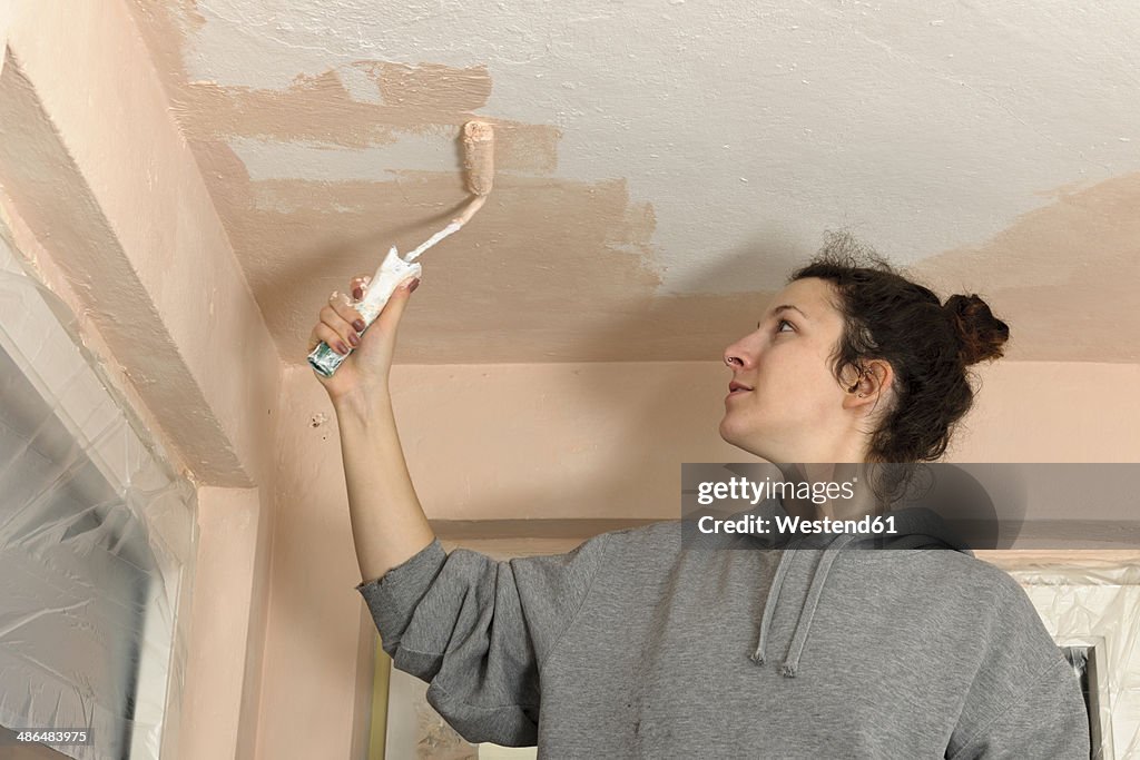 Young woman painting ceiling of an apartment