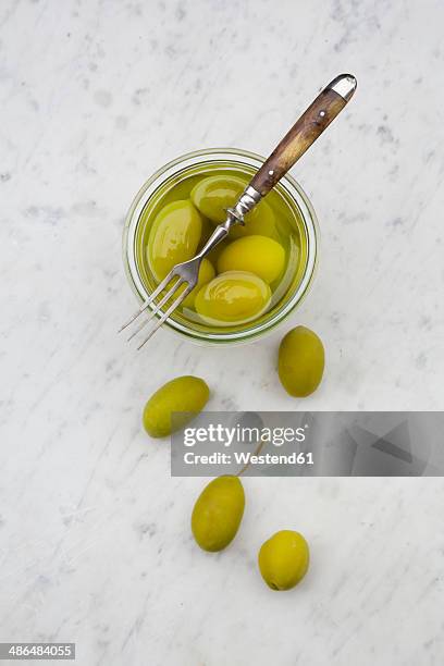 preserving jar of pickled green olives and a fork on white marble, elevated view - green olive fruit stock pictures, royalty-free photos & images