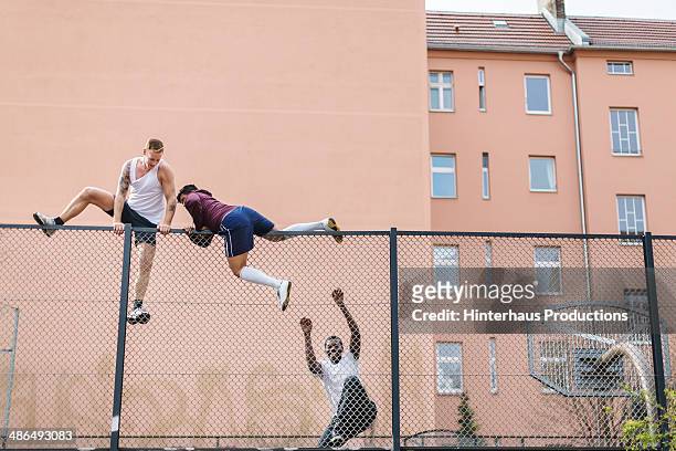 friends climbing over fence - herausforderung stock-fotos und bilder