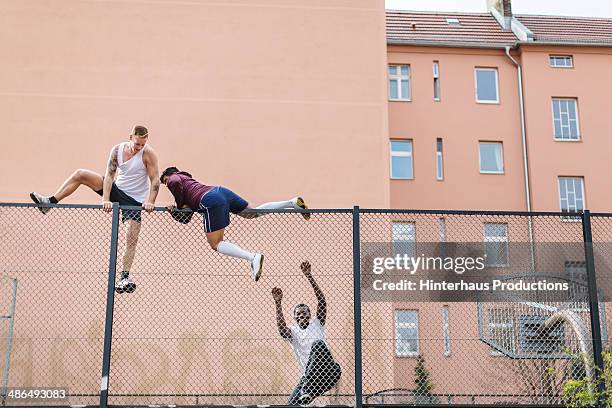 friends climbing over fence - valla límite fotografías e imágenes de stock