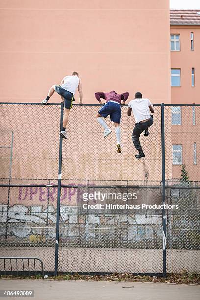 friends climbing over fence - herausforderung stock-fotos und bilder
