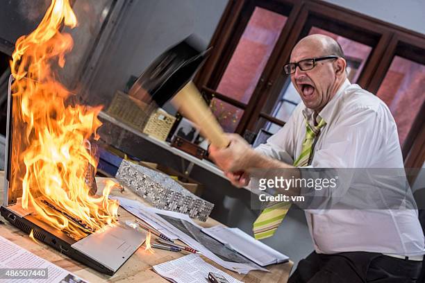 mature adult businessman smashing laptop on fire with hammer - gesloopt stockfoto's en -beelden