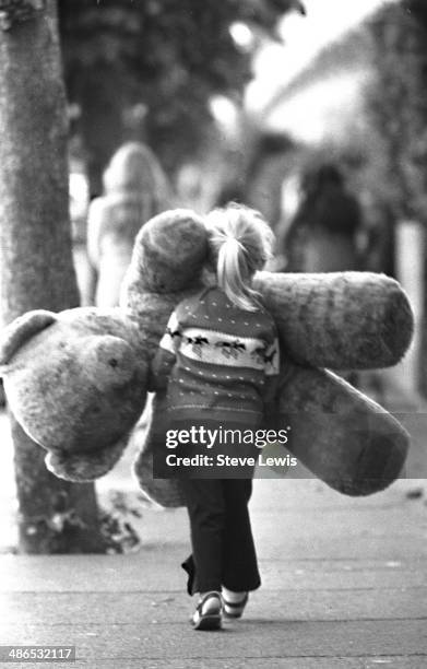 Returning from the fun fair in the East End of London during the 1960s, a young girl is matched for size by a soft toy she has won.