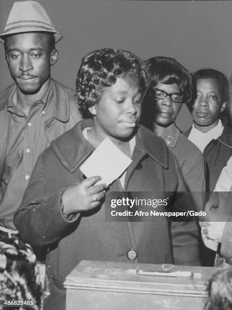 Group of African-American voters stand in line while a woman places her ballot into a ballot box, Baltimore, Maryland, November 10, 1964.