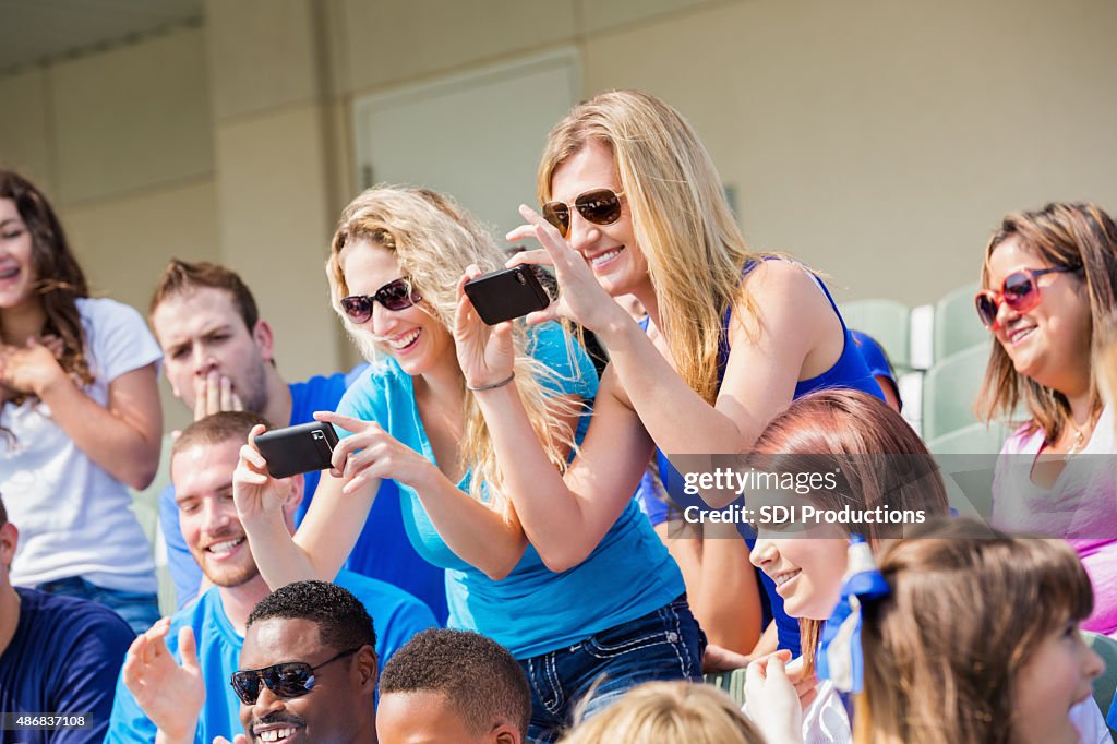 Excited sports fans taking photos during sporting event in stadium
