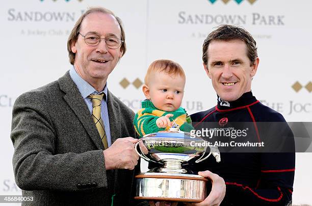 Ex Arsenal footballer Charlie George presents Tony McCoy and his son Archie pose with his trophy for being champion jockey at Sandown racecourse on...
