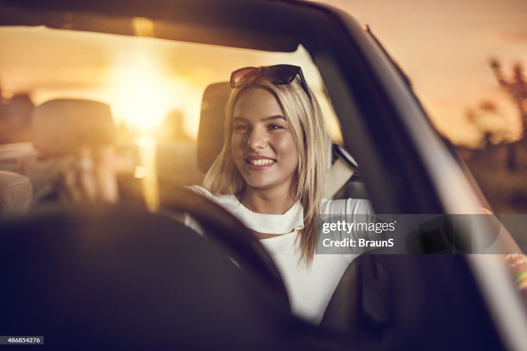 Young happy woman driving a convertible car at sunset.