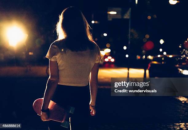 skater girl walking alone with her skateboard at night - rear view girl stockfoto's en -beelden