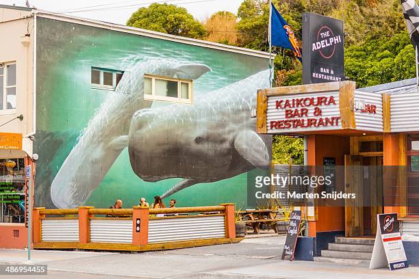 Massive painting of a sperm whale, on a wall at Kaikoura Bar & Restaurant located on West End. Bunch of people on a terrace having a beer.