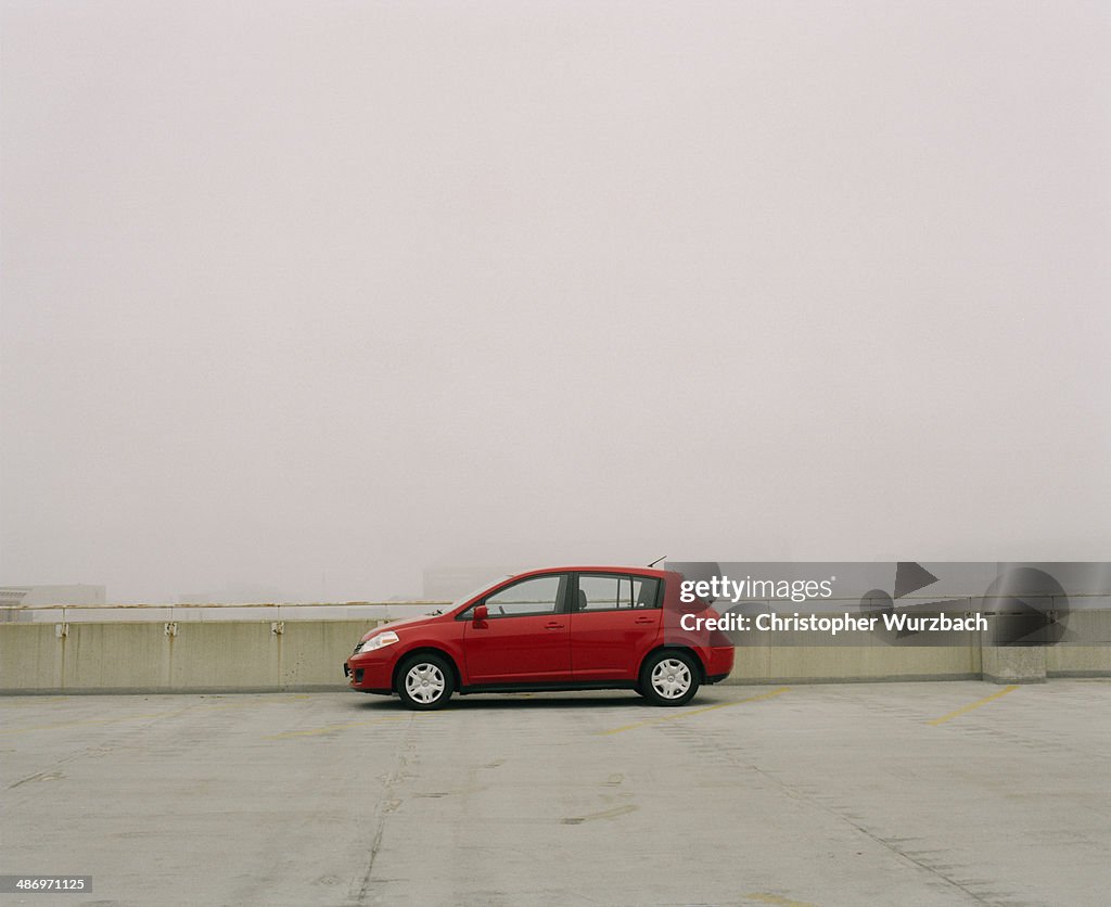 Red compact car on top of parking garage in fog