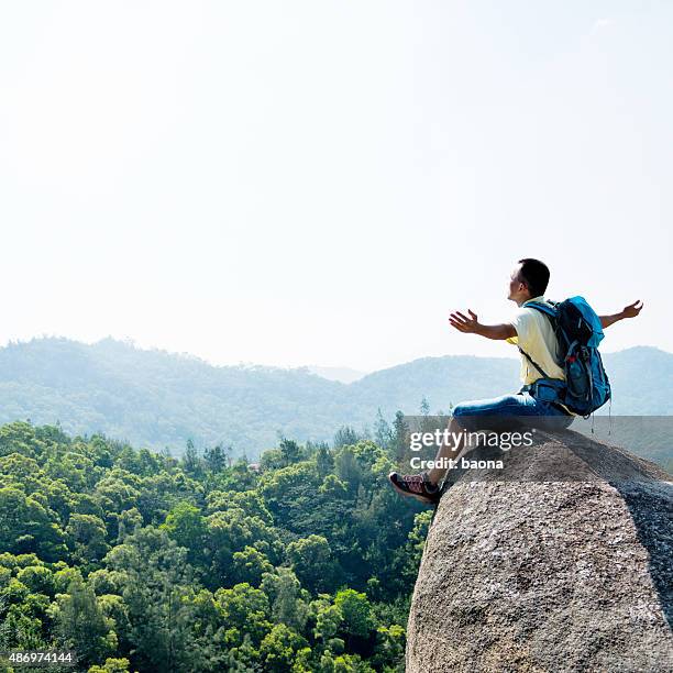 männliche rucksacktourist sitzt auf ledge - happy male side view stock-fotos und bilder