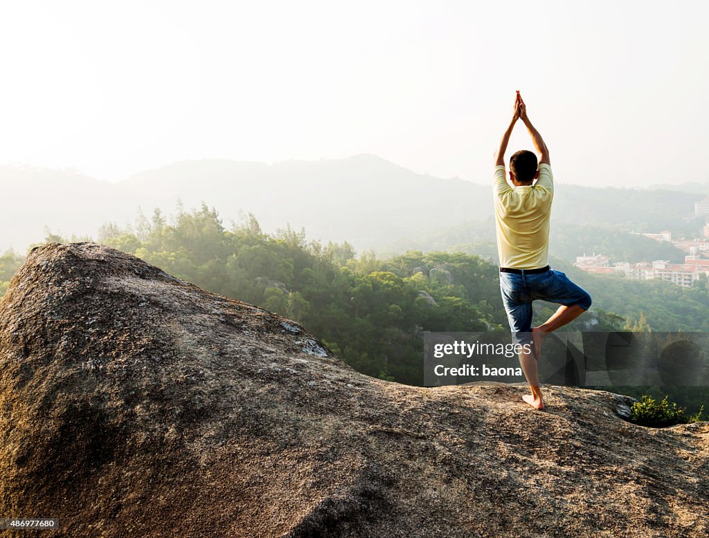 Asian man doing yoga on mountain peak