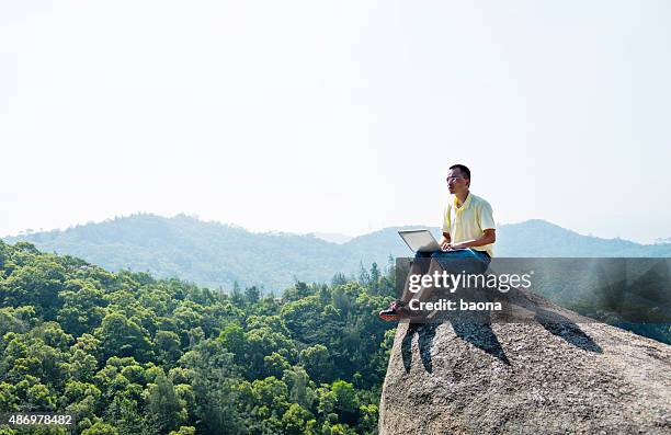 asian man using laptop on rock - laptop remote location stock pictures, royalty-free photos & images