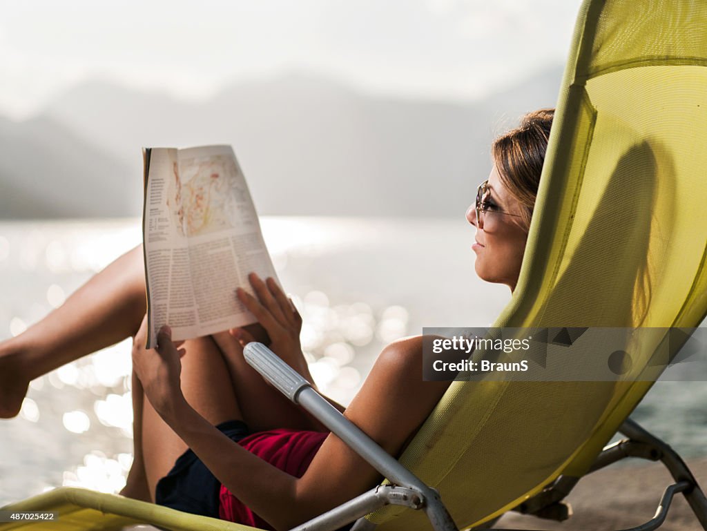 Smiling woman reading a magazine in deck chair.