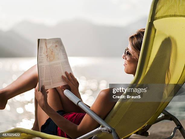 smiling woman reading a magazine in deck chair. - woman on beach reading stock pictures, royalty-free photos & images