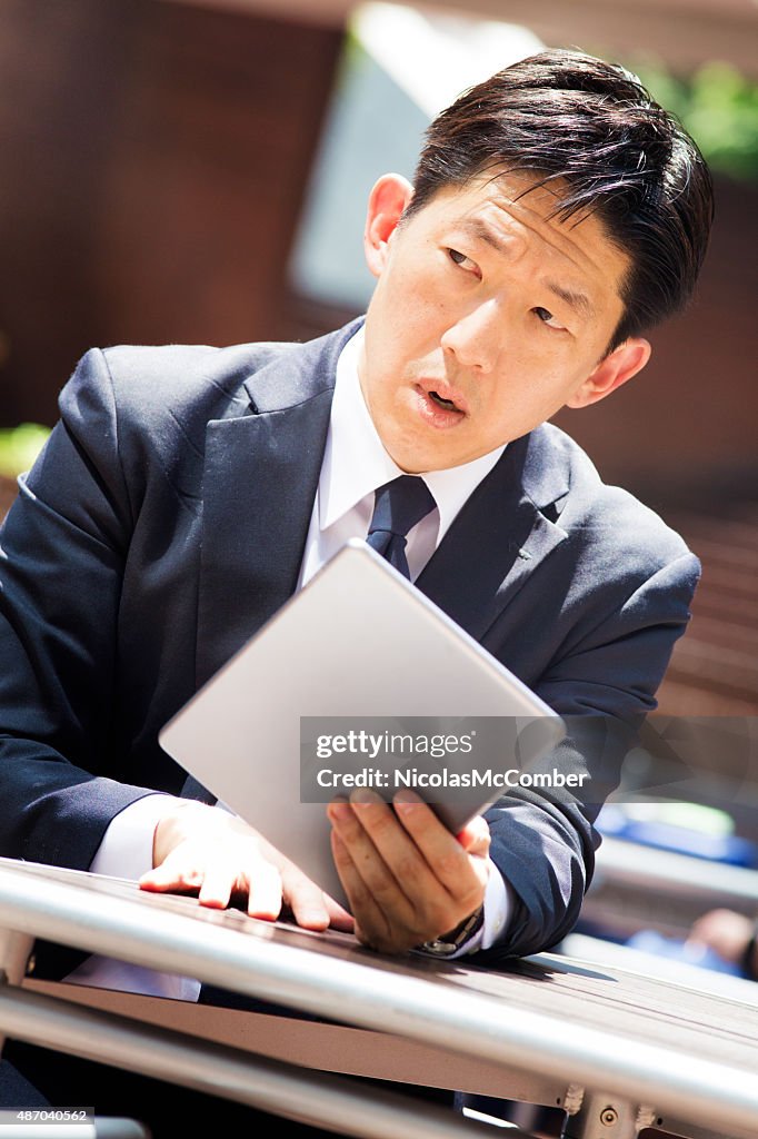 Homme d'affaires japonais looks suspiciously gauche en ligne fondée sur une tablette