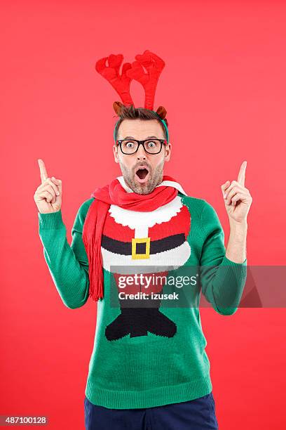 surprised nerd man in funny winter outfit against red background - christmas sweater stockfoto's en -beelden