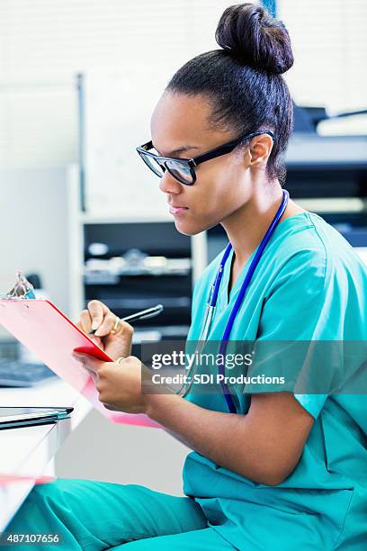 young african american nurse updating patient charts in hospital - clipboard and glasses stock pictures, royalty-free photos & images