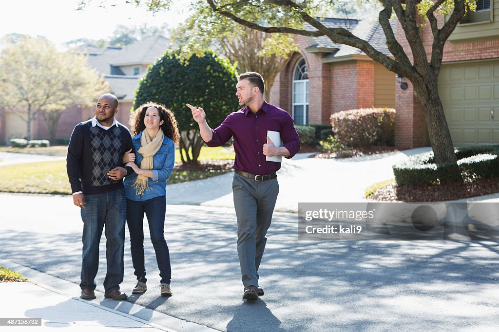 Black couple walking on residential street with agent