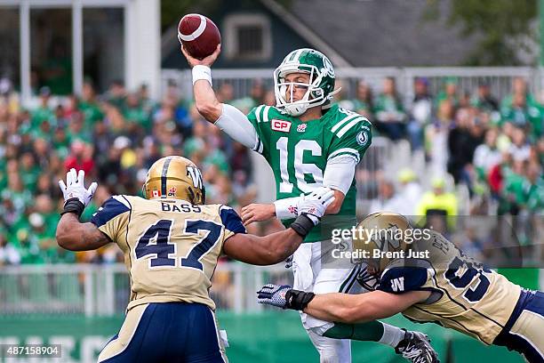 Brett Smith of the Saskatchewan Roughriders throws a pass under pressure from Greg Peach and Khalil Bass of the Winnipeg Blue Bombers in the game...