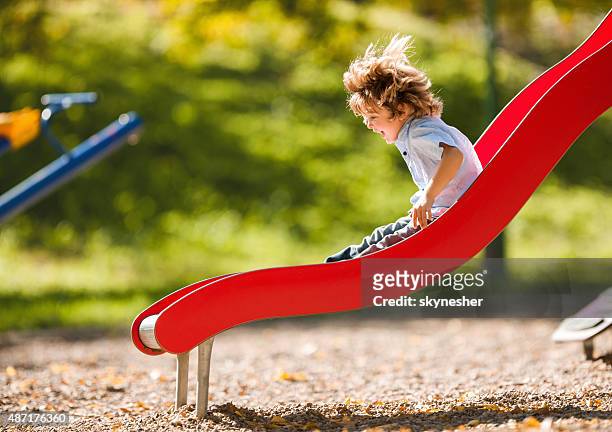 cheerful little boy having fun while sliding outdoors. - playground stock pictures, royalty-free photos & images