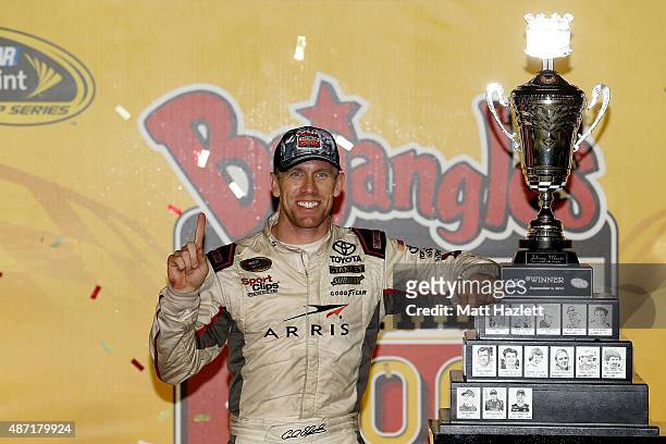 Carl Edwards, driver of the ARRIS Toyota, poses with the winner's trophy in Victory Lane after winning the NASCAR Sprint Cup Series Bojangles'...