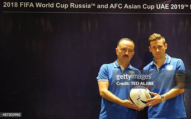 Samvel Babayan , head coach of Uzbekistan poses for photos with player Djeparov Server during a pre-football match press conference in Manila on...