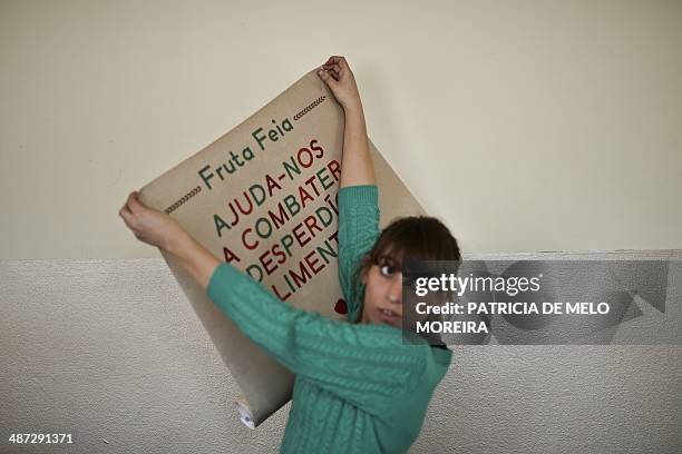 Volunteer pins-up a poster reading "Help us combat food waste" at the "Fruta Feia" co-op in Lisbon on March 17, 2014. The co-op was created over the...