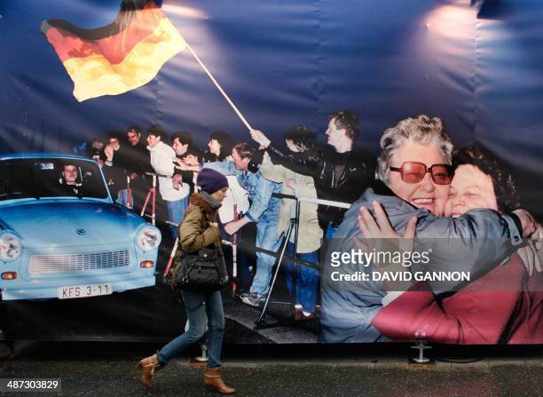 Woman walks past a banner featuring a historic photo of the falling of the wall displayed at Potsdamer Platz in Berlin on November 9 as Germany...