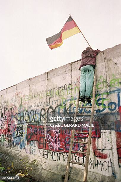 Picture taken 11 November 1989 shows a West Berliner preparing to hand over a FRG flag to East German Vopo policemen through a portion of the fallen...