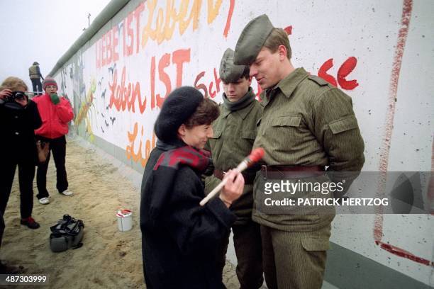 An East German artist offers to paint Vopos' uniforms trying to prevent her from going on painting on the Berlin Wall, on November 21, 1989 in...