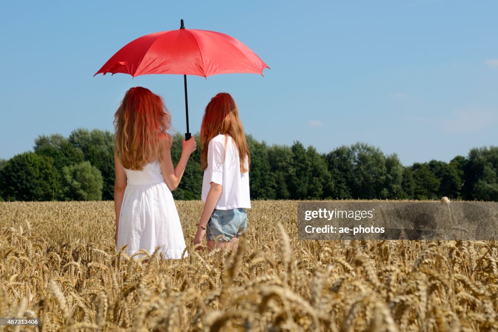 Two teenage girls with red parasol standing in barley field