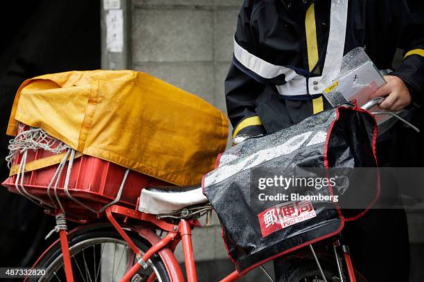 Japan Post Co. Mail pushes his bicycle while delivering mail in Tokyo, Japan, on Tuesday, Sept. 8, 2015. Japan Post Holdings Co. And its banking and...