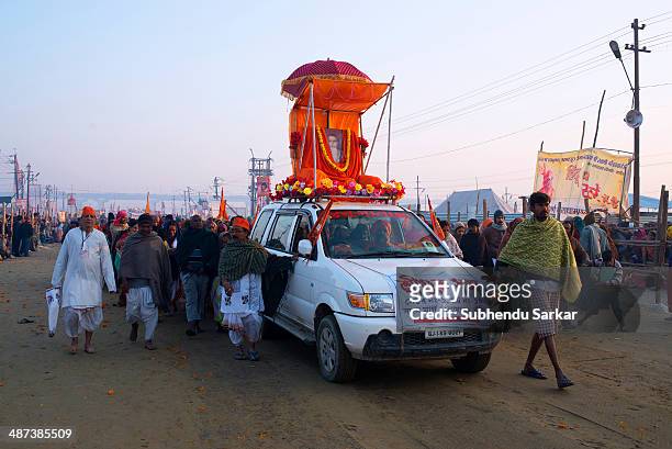 Devotees move towards the confluence of the rivers Ganges and Yamuna beside a car carrying a godman's picture. Kumbh Mela is a site of mass...