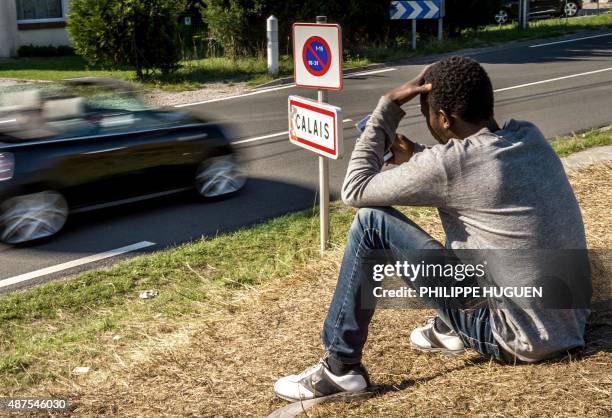 Migrant checks his mobile phone next to a road sign showing the start of the Calais municipality, northern France, on September 10, 2015 in the...