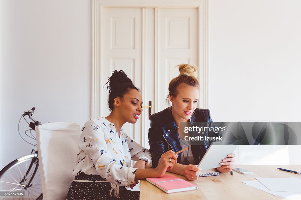 Two women working on digital tablet in an office